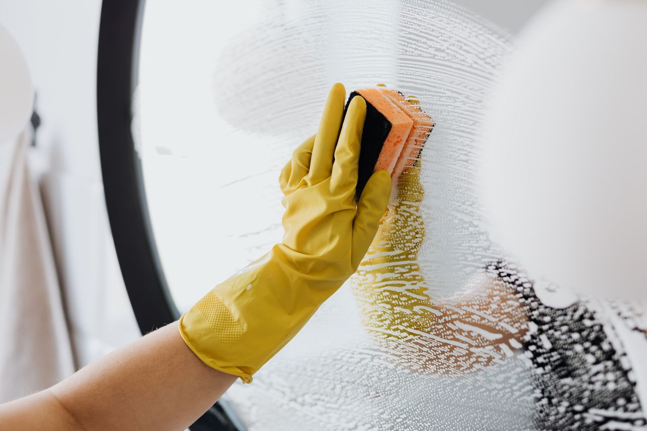 why-choose-us Anonymous person in yellow rubber gloves using simple sponge for cleaning mirror in bathroom