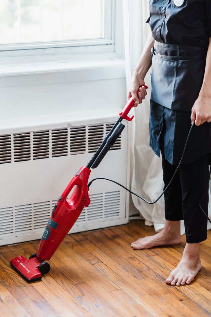 gallery-1 Person cleaning wooden floor with red vacuum cleaner in a well-lit room.