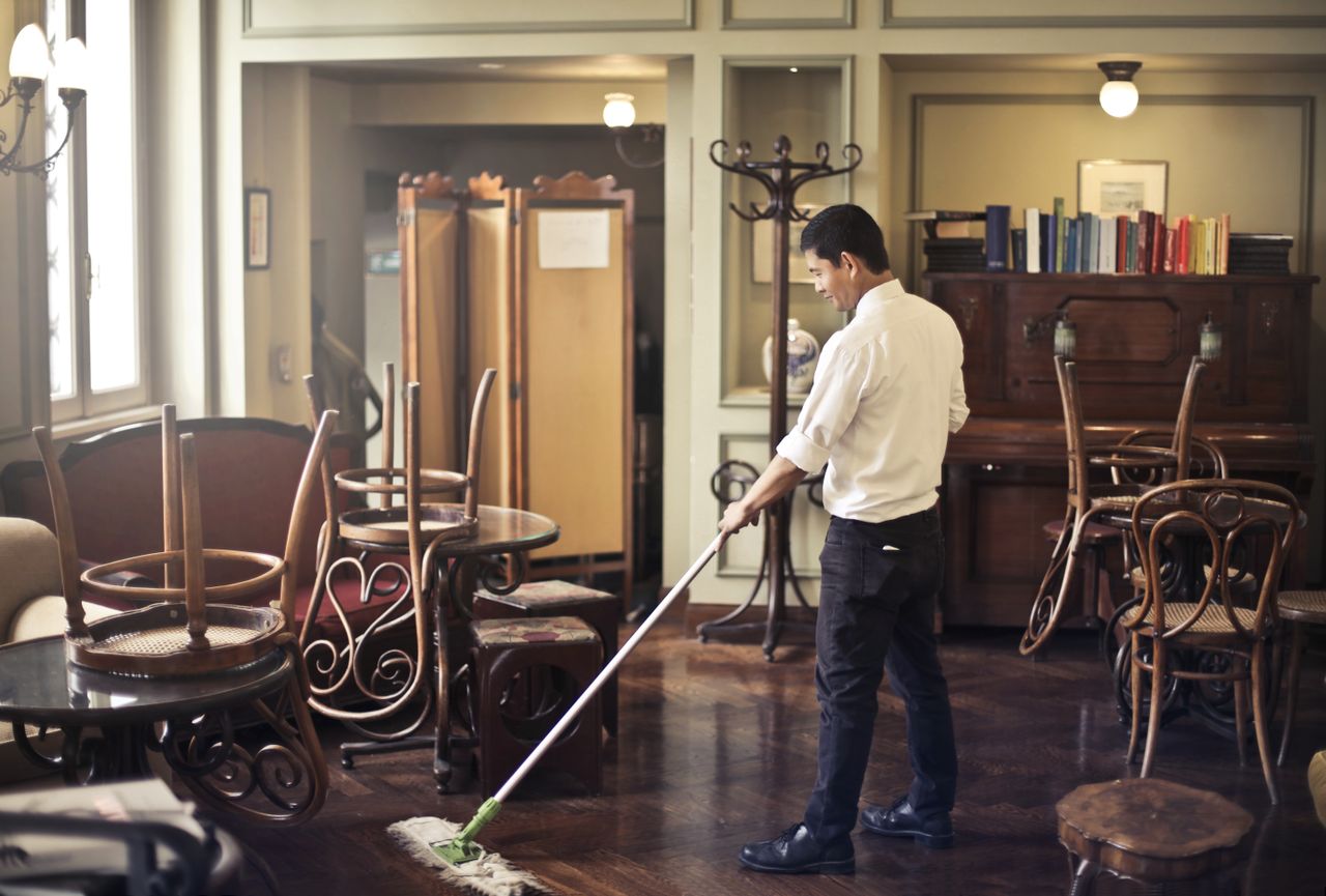 services-02 Side view of young ethnic male in uniform cleaning floor with mop while working in retro styled restaurant